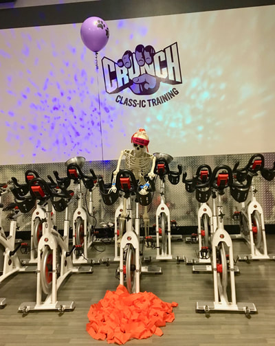 A skeleton in a disco-fan headband rides a spin bike at Crunch.